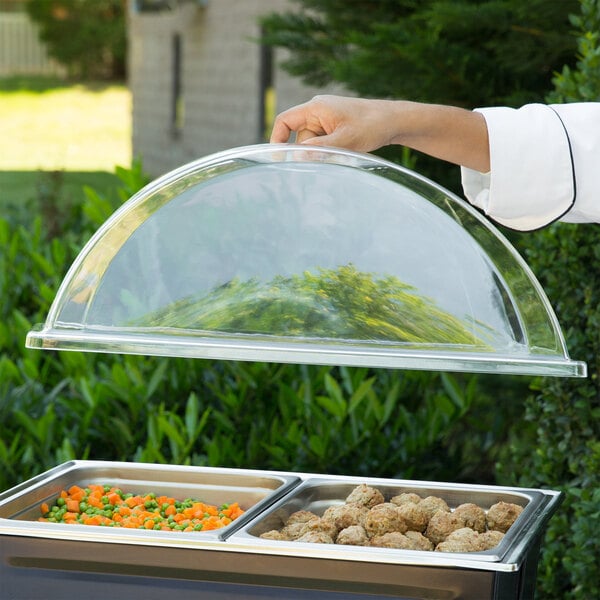 A person holding a clear dome cover over a tray of food.