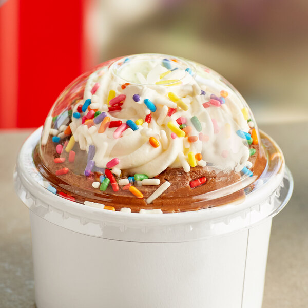 A clear disposable lid on a cup of ice cream with sprinkles.