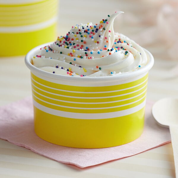 A close up of a yellow paper food cup filled with ice cream and sprinkles.