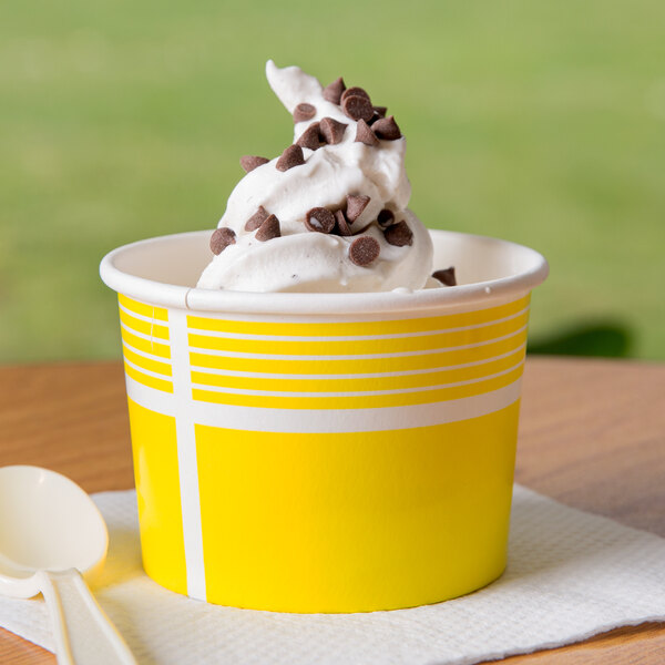 A yellow Choice paper cup filled with white and brown frozen yogurt topped with chocolate chips, with a white spoon.
