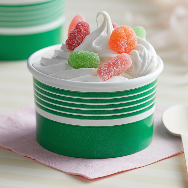 A close up of a green Choice paper cup of frozen yogurt with whipped cream and candy on top.