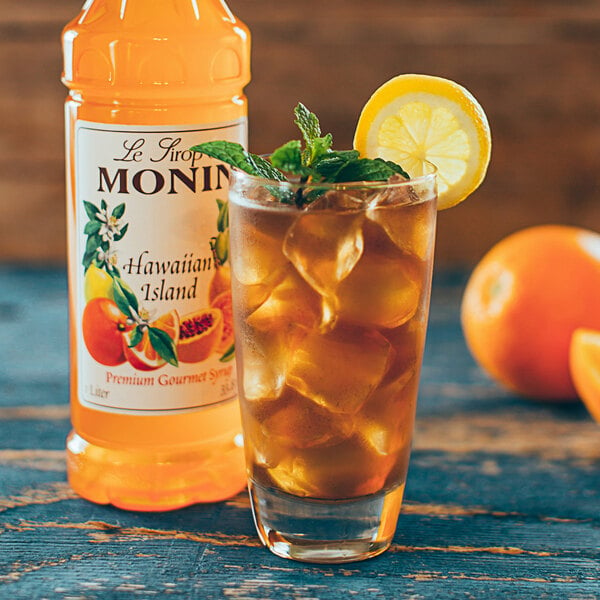 A bottle of Monin Hawaiian Island Flavoring syrup next to a glass of iced tea with a lemon slice and mint leaves.