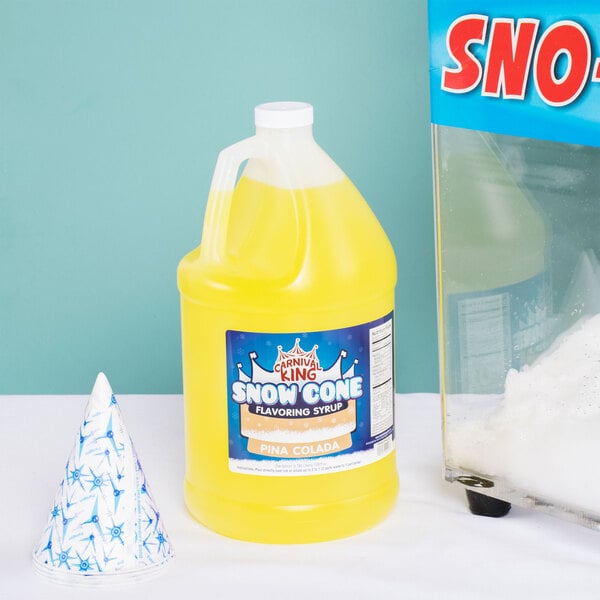 A bottle of yellow Carnival King Pina Colada Snow Cone Syrup next to a glass of snow.