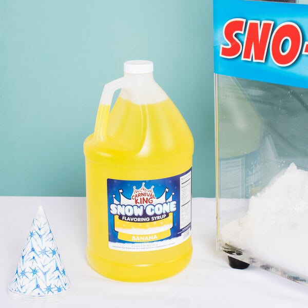 A container of Carnival King Banana Snow Cone Syrup next to a snow cone.