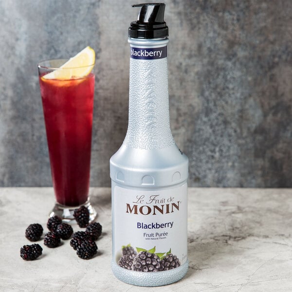 A white Monin bottle of blackberry puree next to a glass of red liquid.