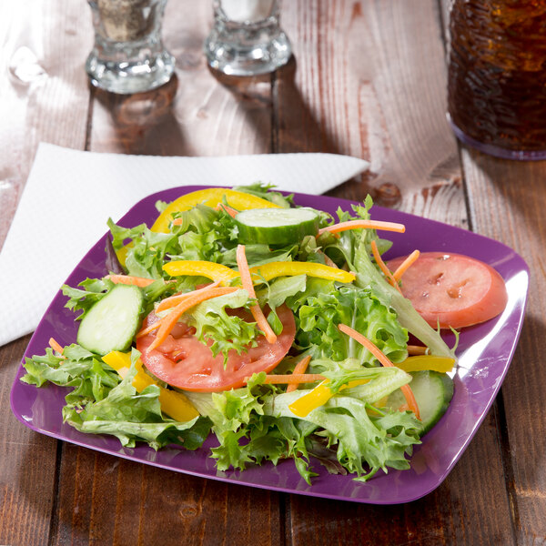 A purple Fineline square plastic salad plate with salad on a table.