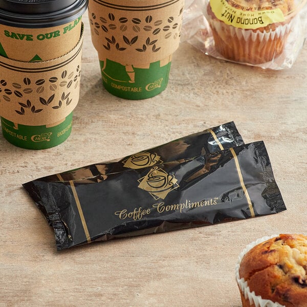 A black and gold Double Serving Hot Beverage Condiment packet next to a coffee cup and muffin.
