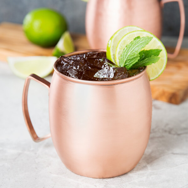 A Clipper Mill brushed copper Moscow Mule mug filled with ice and a drink garnished with lime slices.