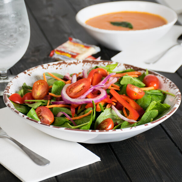 A French Mill melamine bowl filled with salad on a table with a glass of water.