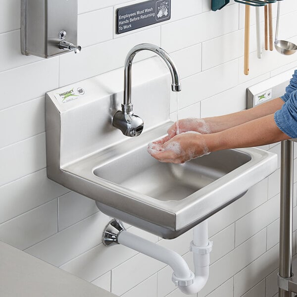 A person washing their hands in a Regency wall mounted hand sink under a faucet.