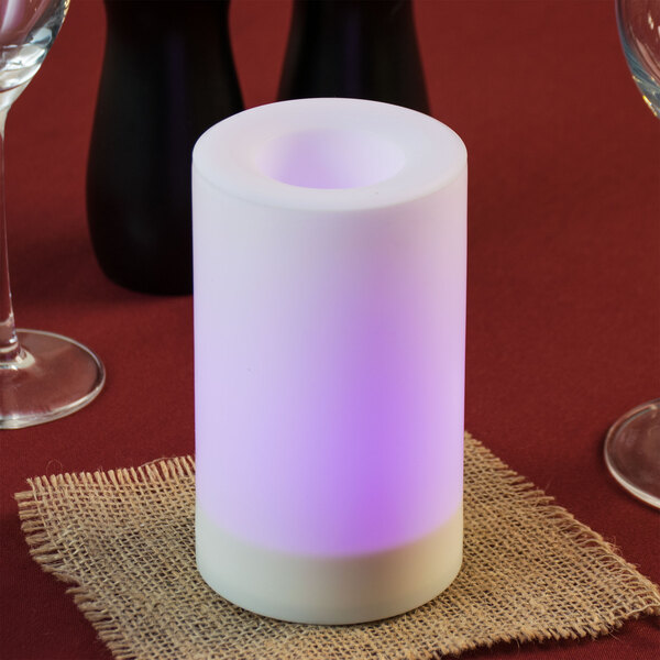 A white Sterno flameless candle with a color changing feature on a table with a burlap napkin and wine glasses.