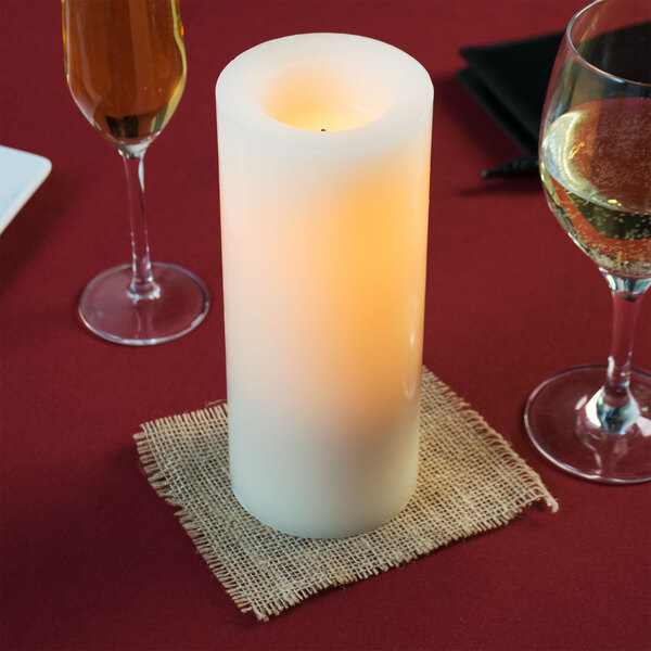 A Sterno cream flameless wax pillar candle on a table with wine glasses.