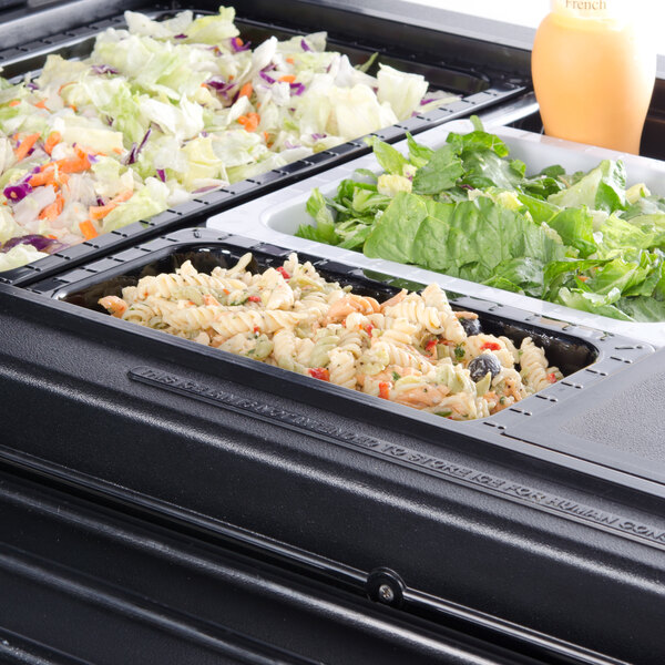 A black melamine 1/3 size food pan with salad in it on a table.