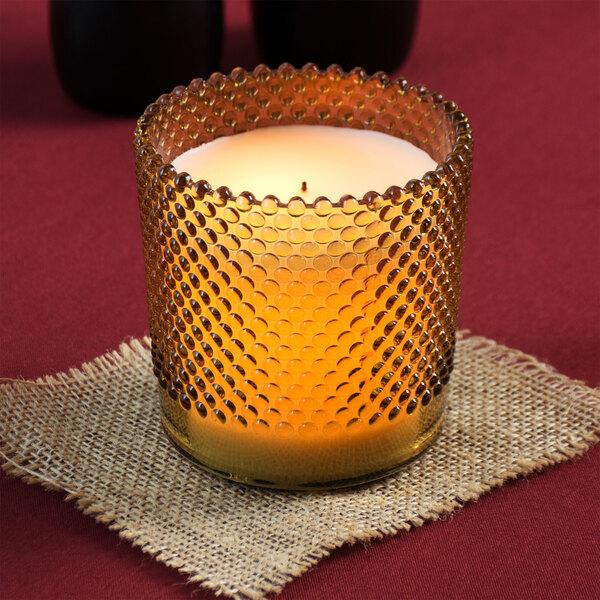 A Sterno amber flameless wax filled glass lamp with a hobnail design and a gold rim on a table.