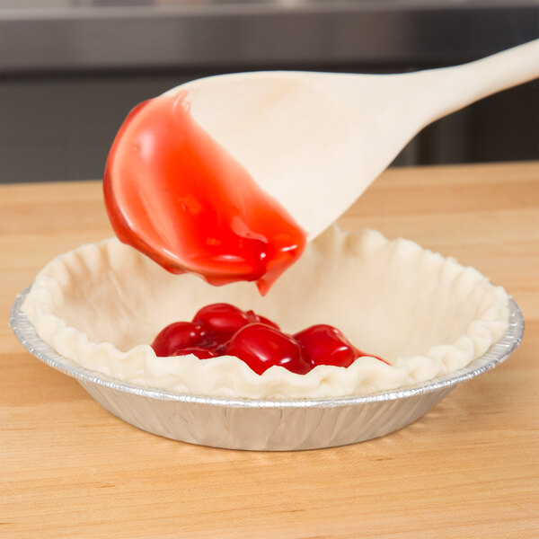 A wooden spoon pouring red liquid into a shallow pie pan.