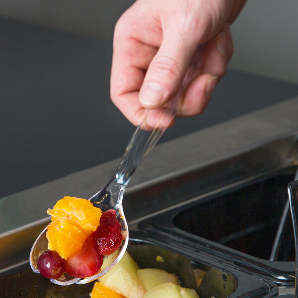 A hand using a Sabert clear plastic serving fork to serve fruit