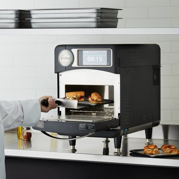 A chef in a professional kitchen using a TurboChef Sota rapid cook oven to bake food.