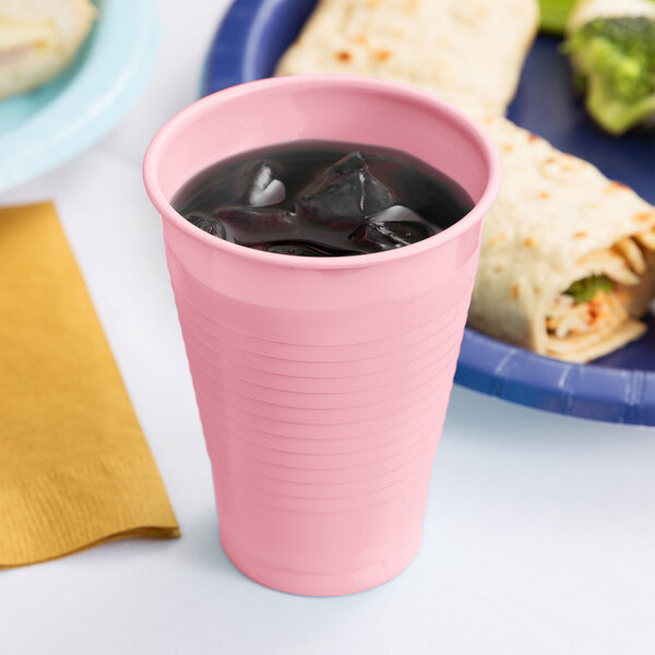 A pink plastic cup with ice in it next to a plate of food.