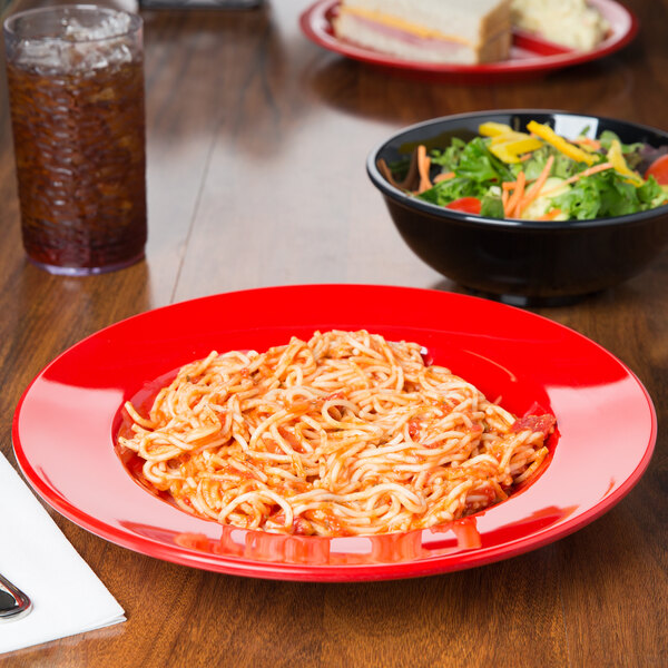 A red GET melamine bowl filled with spaghetti and salad on a table.