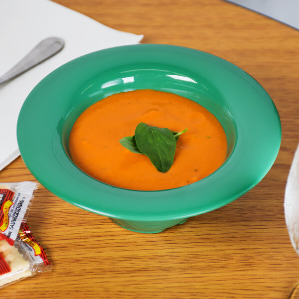 A bowl of soup with a leaf on top sits on a table.