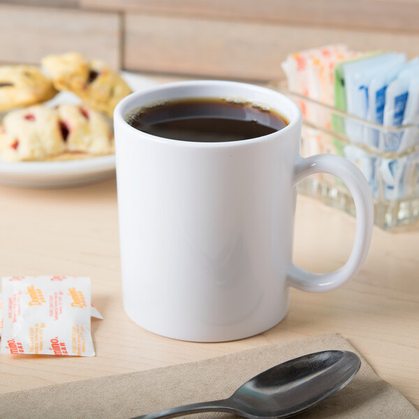 A white GET Tritan mug filled with brown coffee on a counter with pastries.