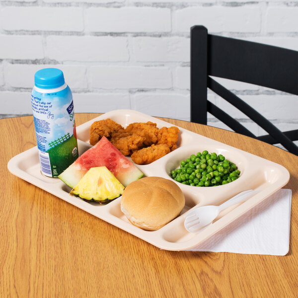 A tan polypropylene compartment tray with food including a roll and vegetables on a table.