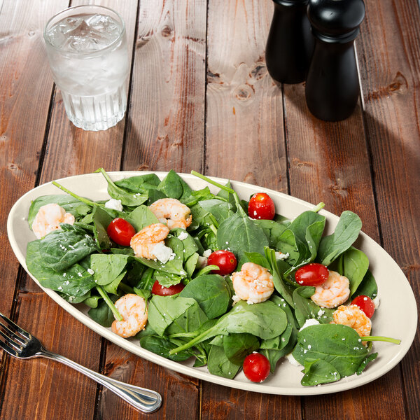 An ivory oval melamine platter with a salad of shrimp and tomatoes on it.
