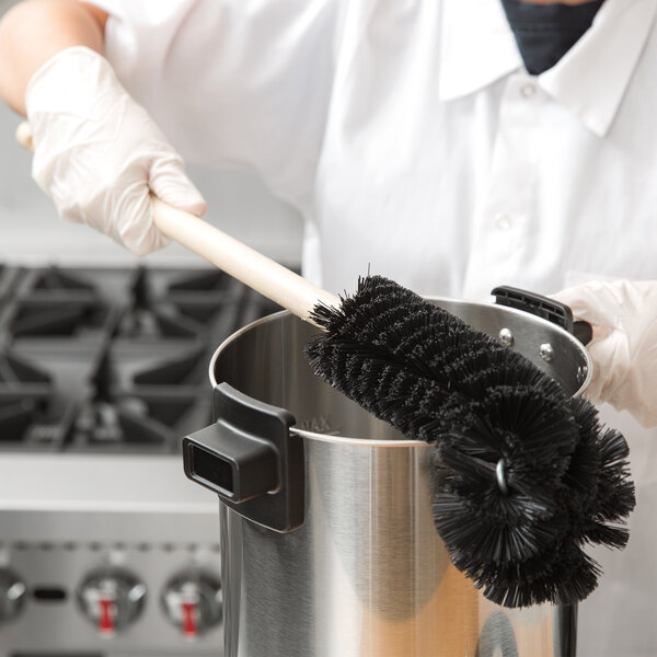 A person using an Urnex angled coffee urn brush to clean a pot.