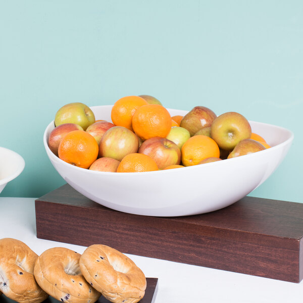 A white Osslo melamine bowl filled with apples and oranges on a table.