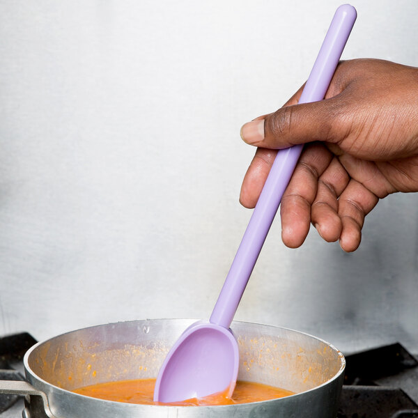 A person holding a purple Mercer Culinary Hell's Tools mixing spoon and stirring food in a pot.