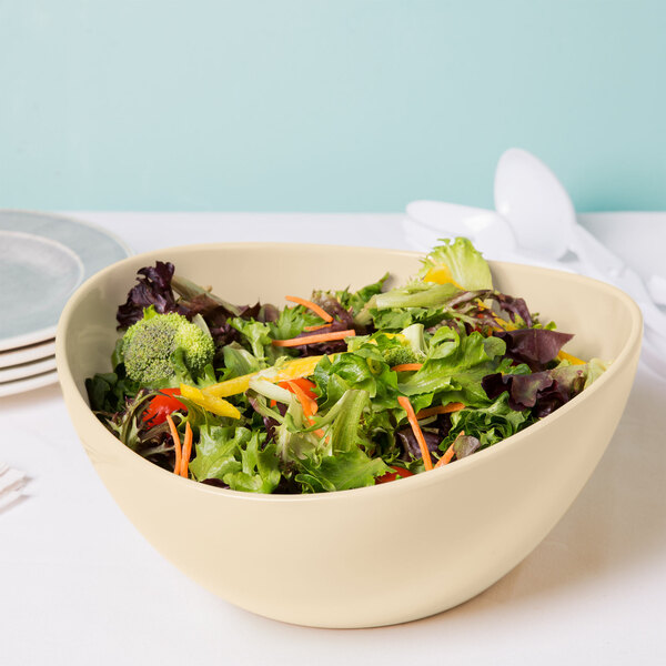 A close up of a Manila melamine bowl filled with salad with vegetables.