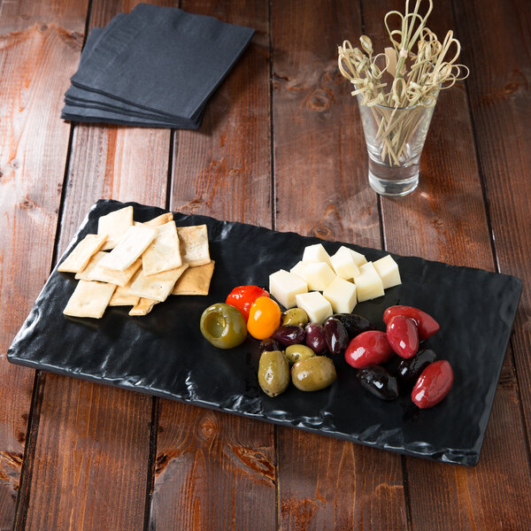 A GET black faux slate display board with olives, cheese and crackers on a counter.