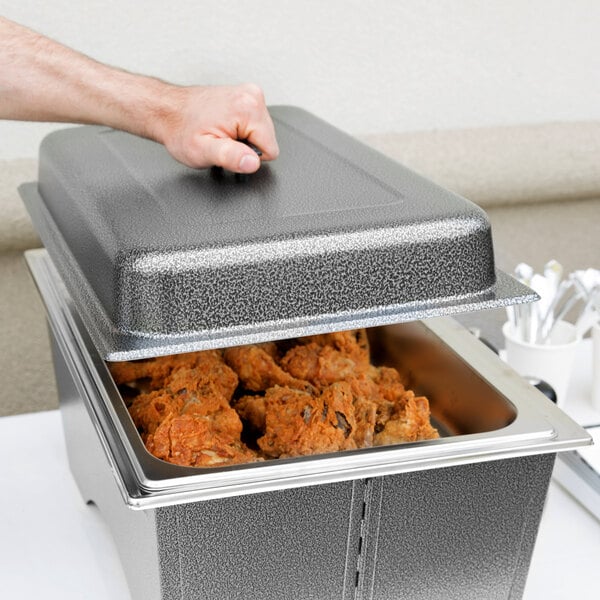 A person holding a Sterno Full Size Silver Vein Fold Away Chafer lid over food.