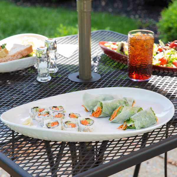 A table with a platter of sushi rolls and a drink on a table outdoors.
