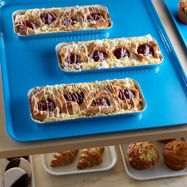 A blue Cambro market tray of pastries on a table.