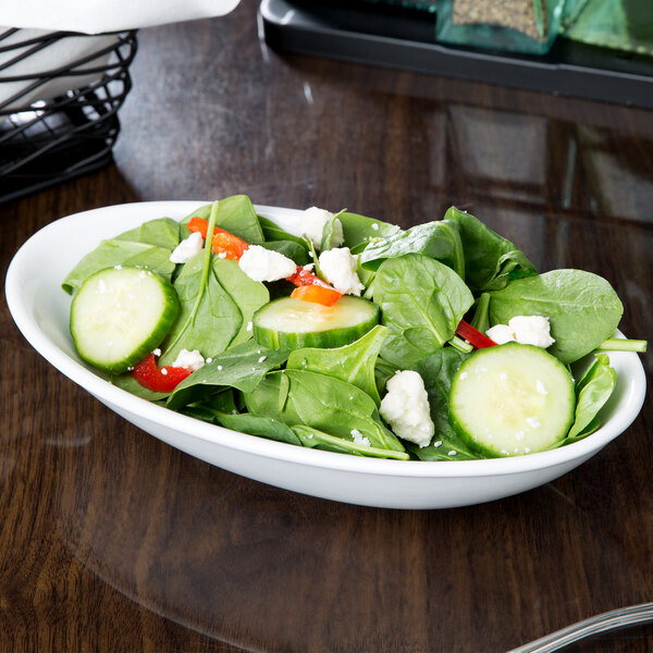 A Libbey Porcelana Infinity white porcelain bowl filled with salad with cucumbers, tomatoes, and spinach.