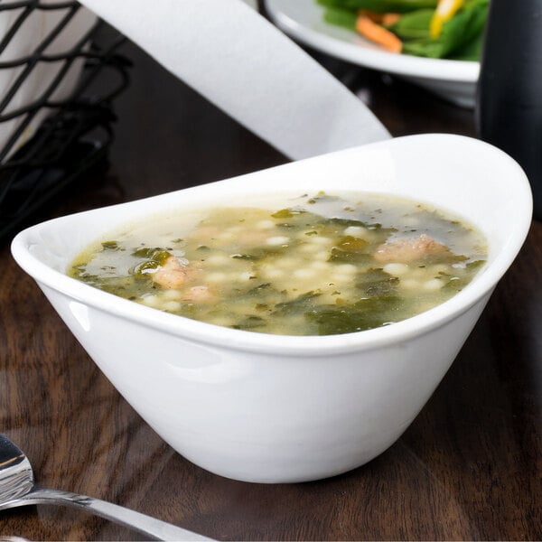 A Libbey Infinity bright white oval porcelain bowl filled with vegetable soup on a table.