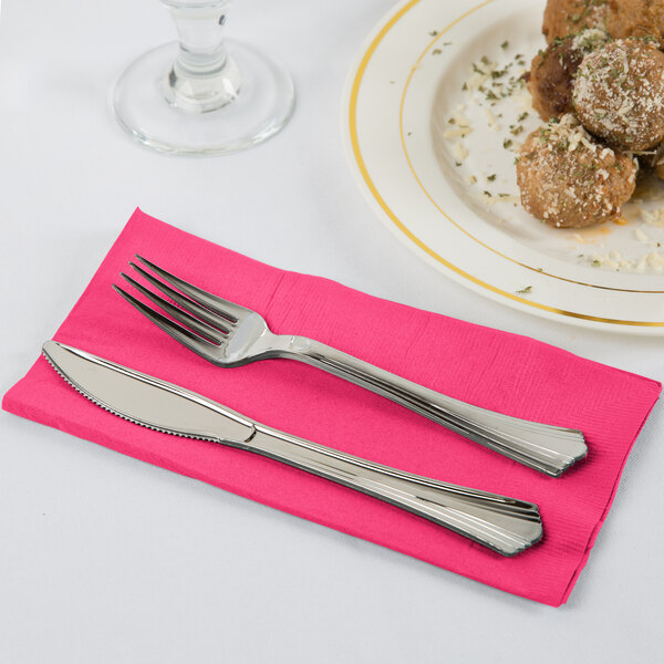 A fork and knife on a Creative Converting Hot Magenta Pink paper napkin.