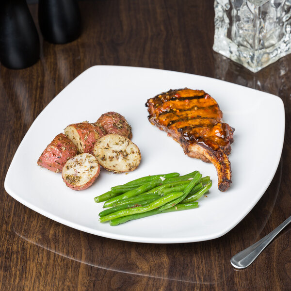 A Libbey Porcelana square porcelain coupe plate with a steak, potatoes, and green beans on a table.