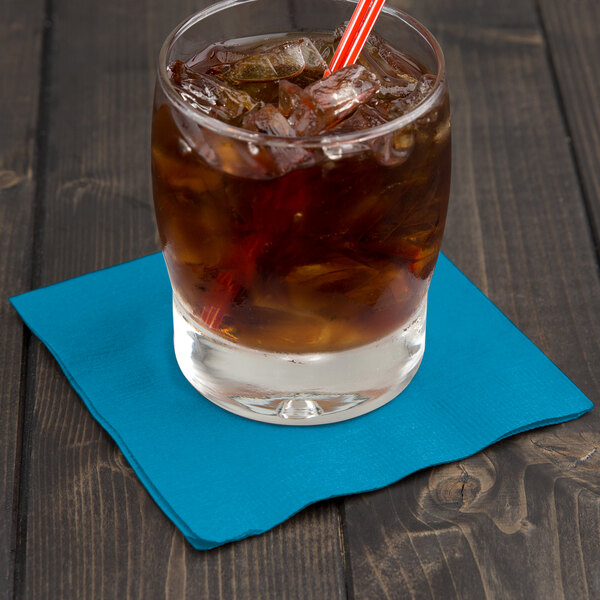 A glass of iced tea with a turquoise beverage napkin and a straw on a table.