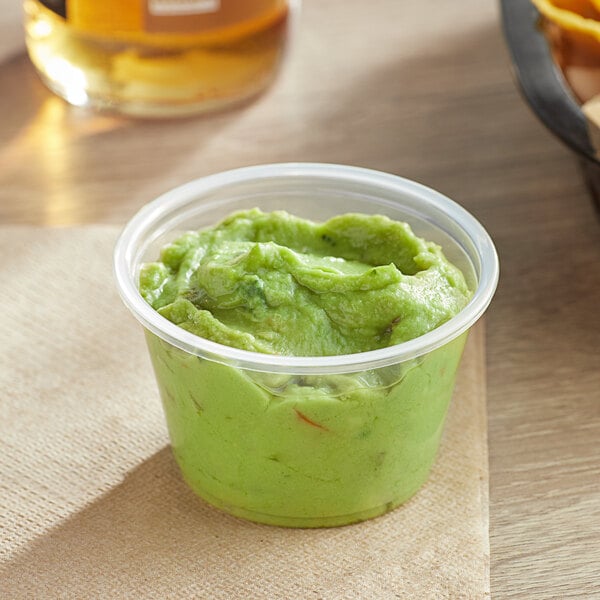 A clear plastic Choice souffle cup filled with green food on a table in a Mexican restaurant.