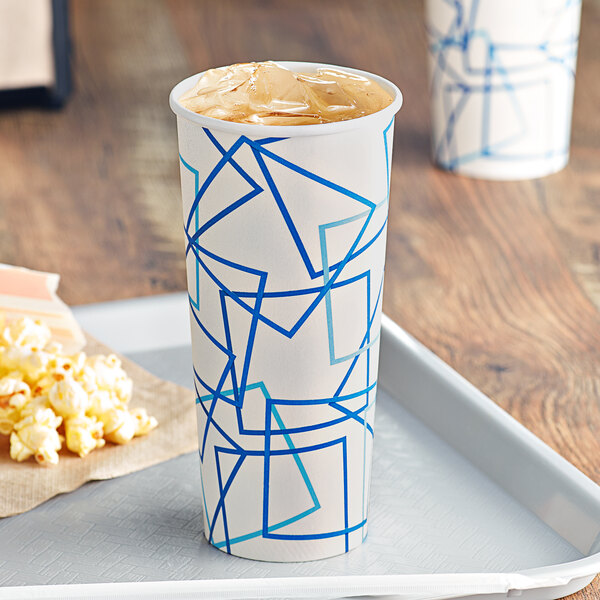 A white cylindrical Choice paper cold cup with a blue and white label filled with soda and ice on a tray with popcorn.