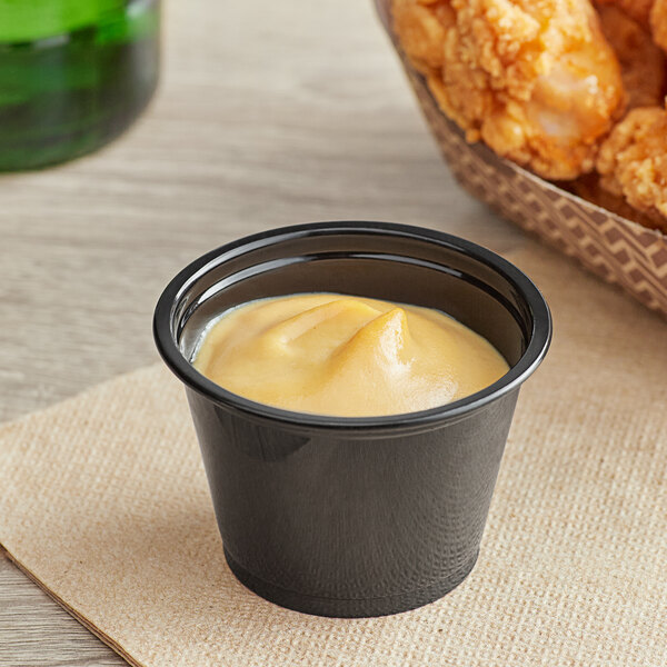 A black plastic Choice souffle cup with yellow liquid in it.