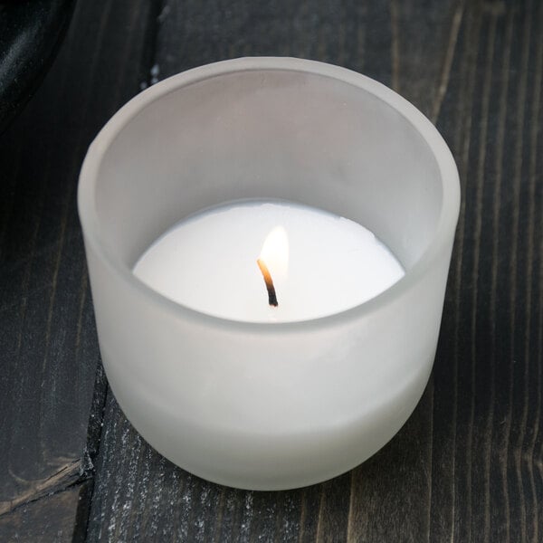 A Sterno PetiteLites white wax candle in a glass container on a table.