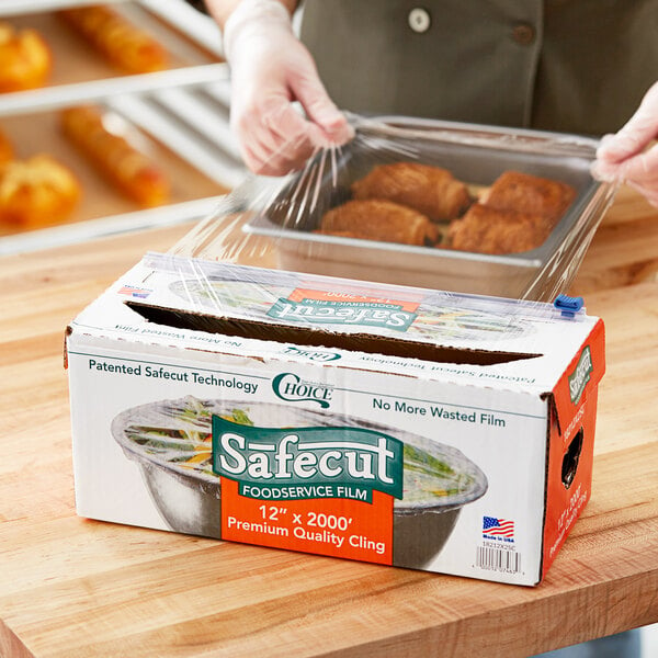 A person using Choice Safecut Premium Foodservice Film on a tray of food on a counter.