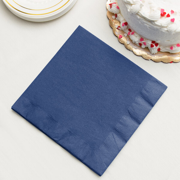 A navy blue Creative Converting paper napkin next to a cake.