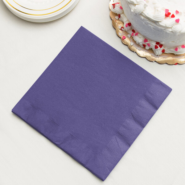 A purple Creative Converting paper dinner napkin next to a white cake.