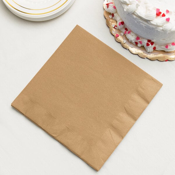 A brown Creative Converting 3-ply paper napkin next to a plate of cake.
