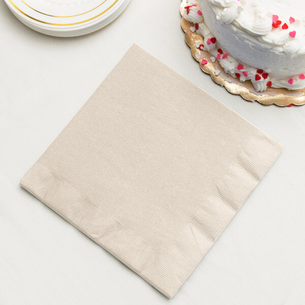 An ivory Creative Converting paper dinner napkin next to a white cake with red sprinkles.