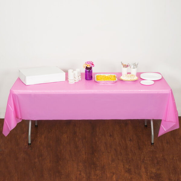 A table with a Candy Pink Creative Converting plastic tablecloth and food on it.